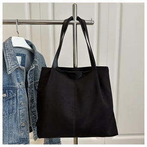 Large black canvas tote bag hanging on a metal rack next to a blue denim jacket