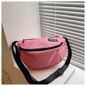 Detail view of pink nylon crescent bag with adjustable strap and fashion label on white stand