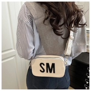 Détail d'un sac bandoulière crème avec logo SM noir et large sangle à motifs