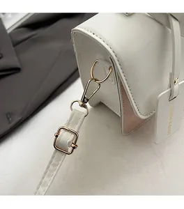 Detail of gold metal hardware and pink leather trim on a stylish white crossbody bag
