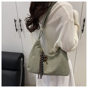 Detail view of sage green hobo bag with fringe and key pendant worn as a shoulder bag