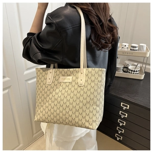 Close-up of the monogram tote bag showing the fashion logo plate and shoulder strap detail