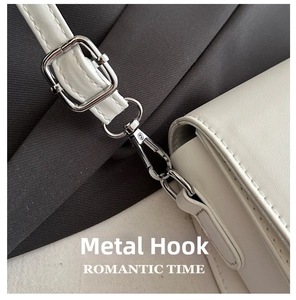 Detailed view of silver metal hook and adjustable strap on a white leather saddle bag