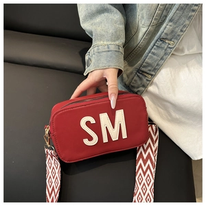 Détail du sac bandoulière rouge avec lettre SM et large sangle en toile à motifs