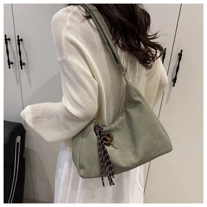 Detail of green crescent tote bag featuring striped tassel charm and matte finish texture