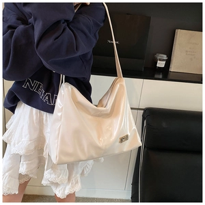 Detail of a creamy white glossy hobo bag featuring a golden logo plate and shoulder strap