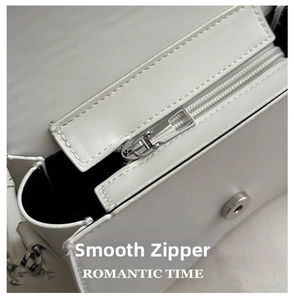 Detailed close-up of smooth silver zipper and magnetic snap on white leather bag