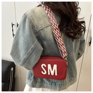 Détail d'un sac bandoulière rouge avec logo SM et large sangle géométrique