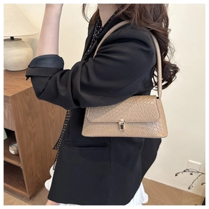 Détail du sac baguette kaki à texture lézard porté par un mannequin sous lumière douce