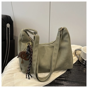 Olive green suede shoulder bag with retro key charm shown in a cozy cafe setting