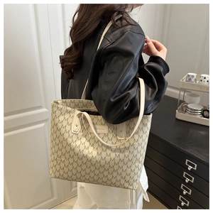 Detail of beige tote bag featuring black M letter monogram and rectangular fashion badge