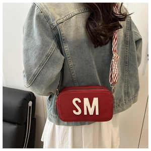 Sac bandoulière rouge carré tendance avec large sangle à motif porté par un modèle