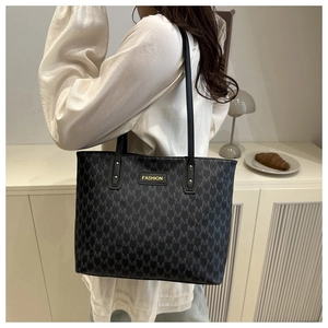 Detail of black monogram tote bag with gold logo patch and slim leather shoulder straps