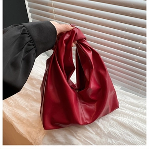 Detail of dark red knotted tote bag with soft pleated texture held by a model