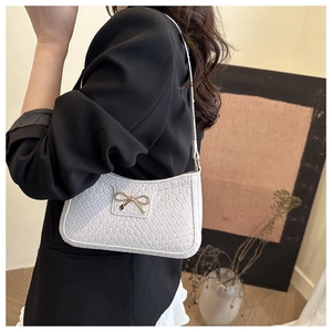 Close-up of white woven pattern underarm bag with a golden bow buckle on a model