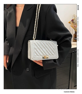 Detail of white quilted crossbody bag with metal chain strap and push-lock closure