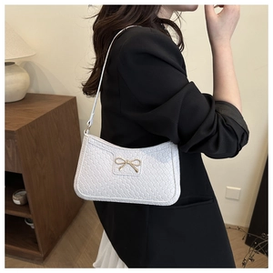 Close-up of white woven leather crescent bag with a gold bow buckle on shoulder