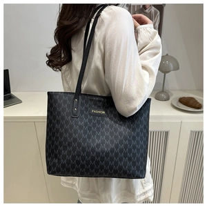 Detail of black tote bag with M-pattern print and gold fashion metal plaque on shoulder