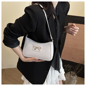 Detail of white woven underarm bag featuring a delicate golden bow metal accent