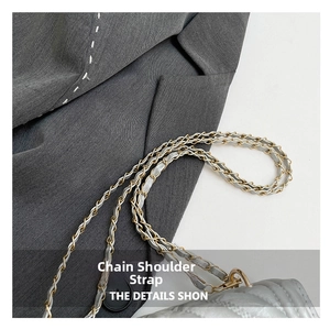 Macro view of woven metal and leather chain strap on grey quilted square shoulder bag