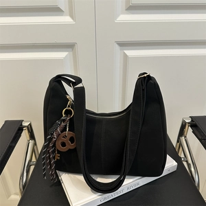 Minimalist black hobo tote bag with gold zipper and stylish cookie charm on a chair