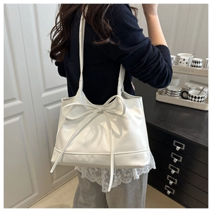 White shoulder bag featuring a large decorative bow and elegant trapezoidal leather design