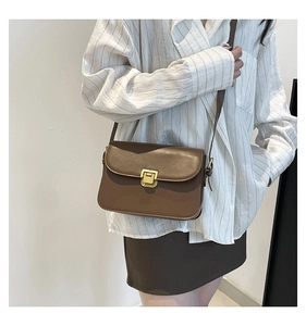 Gros plan d'un sac bandoulière en cuir marron avec boucle dorée sur chemise rayée