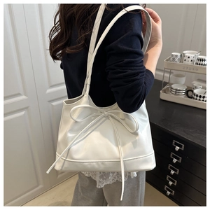 Detail of white leather tote bag featuring a large decorative bow and spacious interior