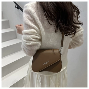 Vue latérale d'un sac besace marron en cuir avec lettrage tendance sur un escalier blanc