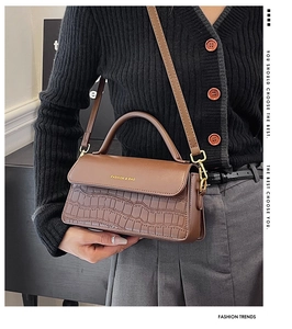 Detail of dark brown stone textured handbag with gold letter logo and crocodile pattern