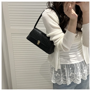 Détail de la texture tressée noire et fermoir doré sur sac baguette vintage épuré