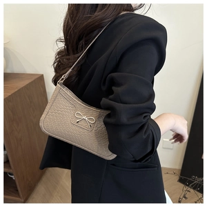 Detail of beige faux crocodile skin bag with silver metal bow buckle on model shoulder