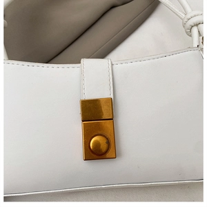 Close-up of the golden rectangular metal buckle on a white leather shoulder baguette bag