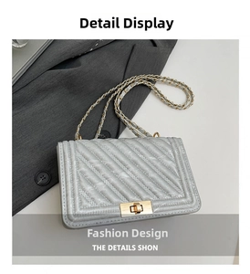 Detail of silver quilted crossbody bag with golden clasp and chain strap on grey blazer