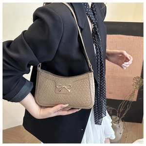 Detail of beige faux leather baguette bag with woven texture and gold bow ornament