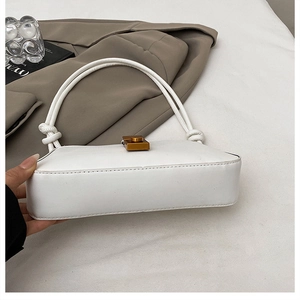 Detail of white PU baguette bag with vintage square metal lock and knotted strap