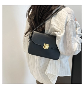 Détail d'un sac bandoulière chic en cuir noir avec boucle dorée porté par un mannequin