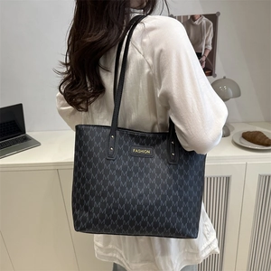 Black large tote bag with M letter pattern and gold logo shown in a minimalist room