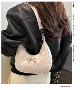 Detail of crocodile embossed cream shoulder bag with golden bow buckle on a leather jacket