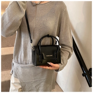 Détail du sac à main noir brillant avec lettrage doré et fine bandoulière élégante