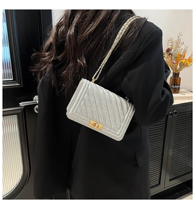 Model wearing a gray quilted flap bag with gold chain strap and metallic push-lock closure