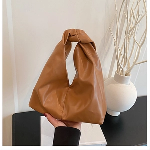 Detail of a brown leather knot-handle hobo bag held by hand in a minimalist setting