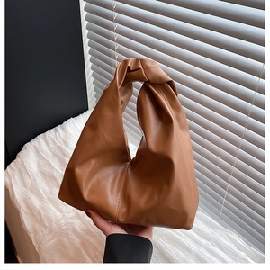 Close-up of caramel brown ruched handbag with trendy knot handle and soft faux leather texture