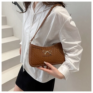 Detailed view of woven texture and gold bow buckle on brown PU leather underarm bag