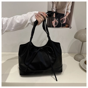 Detail of black tote bag with bow accent and long handles for shoulder or hand carry