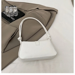 Detail of white leather shoulder bag with knot decoration on a minimalist background