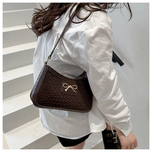 Detailed close-up of dark brown woven underarm bag featuring a delicate gold bow hardware
