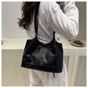 Back view of a black leather tote bag with a bow detail worn over the shoulder