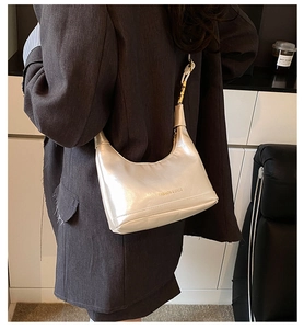 Model wearing a cream-colored pearlescent crescent bag with gold chain strap detail