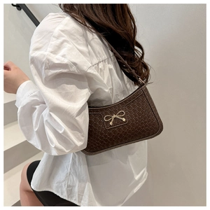 Deep brown croc-effect baguette bag with a gold bow buckle shown on a model's shoulder